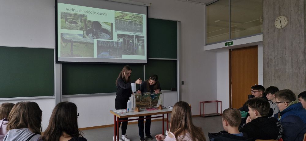Učenka v predavalnici pomaga pri izvedbi poskusa.