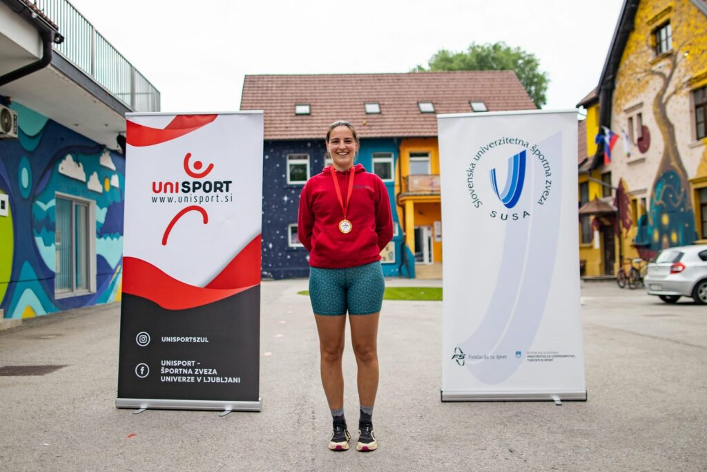 Med promocijskima pingvinoma stoji Teja Tušar. Okoli vratu ima medaljo.