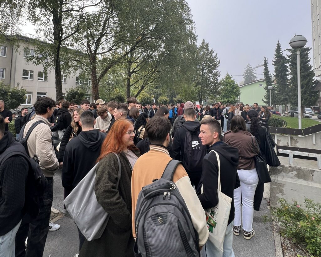 Novi študenti vseh študijskih smeri UL FGG pred pričetkom sprejema bruck in brucev. Študentje stojijo pred fakulteto in se med seboj pogovarjajo.